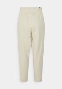 Lys beige joggerbukser lavet af blødt materiale, der har en elastisk talje og indsnævrede ankler, med en glat overflade og uden synlige mønstre.