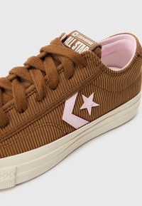 Brown corduroy low-top sneakers with pink logo and star detail, white rubber sole, and brown laces. Smooth inner lining.