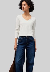 Top bianco a maniche lunghe con colletto a V abbinato a jeans a gamba larga blu scuro a vita alta, dotati di tasche frontali e cuciture a contrasto.
