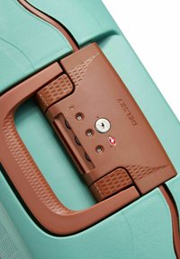 Lys teal koffert med en brun kombinasjonslås. Låsen har teksturerte detaljer og tre tastaturknapper. Glatt overflate, slitesterkt materiale.