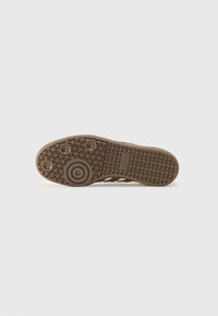 Semelle de sneaker brun clair avec un motif texturé, présentant des accents surélevés circulaires, des grips triangulaires et des sections lisses. Logo de la marque visible.