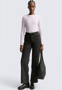 Lichtpaarse geribbelde top met lange mouwen, gecombineerd met wijd uitlopende zwarte jeans met hoge taille. Zwarte enkellaarsjes en een zwarte totebag maken de outfit compleet.