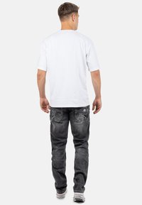 T-shirt bianco a maniche corte con colletto girocollo, abbinato a jeans grigio scuro con tasche posteriori dettagliate e un leggero effetto lavato.