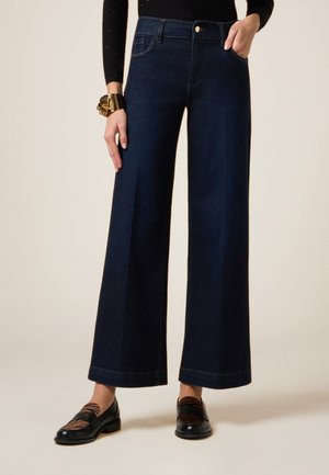 Donkerblauwe wijde jeans hebben een middelhoge tailleband, zijzakken en achterzakken met zichtbare stiksels.