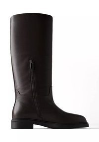 Botte haute en cuir noir avec fermeture éclair latérale, semelle basse plate et bout rond, vue de profil extérieur sur fond blanc.