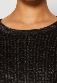 Czarny sweter dzianinowy z fakturowanym wzorem i metalicznymi akcentami. Żebrowany dekolt i szczegółowy design powierzchni.