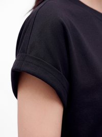 Primer plano de una persona que lleva una camisa negra de manga corta con un detalle de puño doblado en la manga.