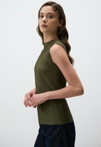 Top senza maniche verde oliva con pieghe verticali, scollatura alta e vestibilità slim. Abbinato a pantaloni in denim scuro, mostrando un profilo laterale.