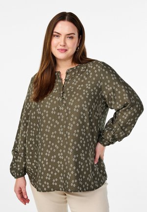 Blusa verde oliva con motivi a diamante e floreali bianchi, caratterizzata da un colletto con bottoni e maniche lunghe ampie e arricciate.