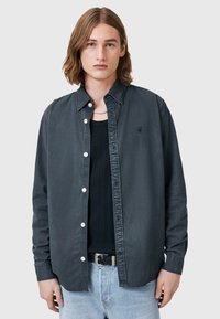 Camicia nera con bottoni, dal tessuto morbido, colletto classico e bottoni bianchi. Indossata sopra una canotta nera a coste e abbinata a jeans in denim chiaro.