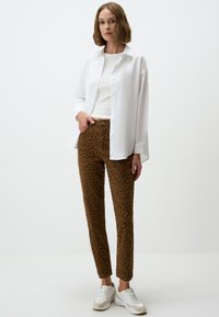 Chemise blanche boutonnée, débardeur blanc ajusté, et pantalon léopard brun associé à des baskets blanches. Tissu lisse et coupe ajustée.
