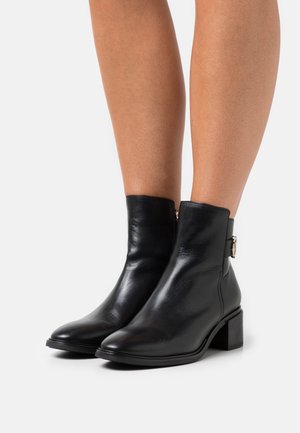 Bottines en cuir noir avec un bout rond, des coutures minimales et une fermeture éclair sur le côté. Elles sont dotées d'un petit talon carré et d'une boucle en métal argenté.