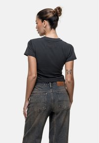 T-shirt nera aderente con maniche corte, con logo in rilievo sul retro. Abbinata a jeans in denim blu sbiadito a vita media con tasche posteriori.