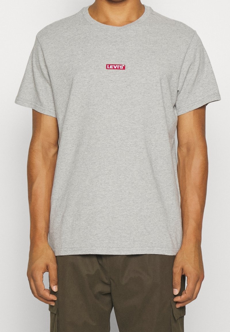 Homme portant un t-shirt gris clair à manches courtes avec un petit logo rouge Levi's sur la poitrine et un pantalon cargo vert olive foncé.