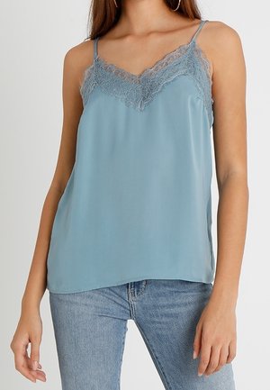 Kvinde iført lyseblå satin cami med blonder og tynde stropper, kombineret med lyseblå cowboybukser.