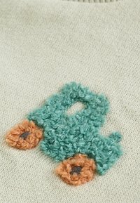 Gesticktes grünes Lastwagen-Design auf einem hellbeigen Stoff, mit flauschiger Textur und orangefarbenen Radakzenten mit braunen Mittelpunkten.