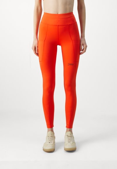 High-waisted, orange leggings with pockets, made from stretchy material. Features logo text "7 DAYS ACTIVE" on the lower leg.
