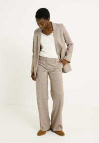 Traje de dos piezas a cuadros en colores apagados, con un ligero patrón de cuadros. Los pantalones son de pierna ancha, combinados con una blusa blanca con encaje.