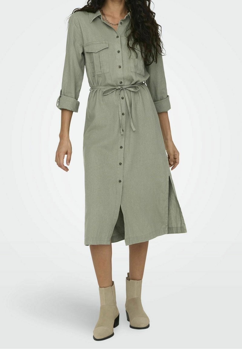 Abito camicia verde chiaro con maniche lunghe, chiusura con bottoni, due tasche sul petto e cintura in vita, caratterizzato da uno spacco laterale e tessuto testurizzato.
