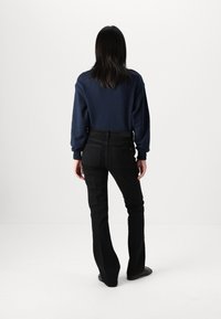 Navy sweatshirt, black flared jeans, smooth texture, simple design. Jeans have back pockets; person facing away from the camera.