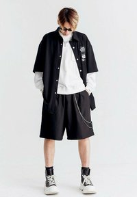 Camisa negra de manga corta y con botones, sobre un sudadera de cuello redondo blanca, combinada con pantalones cortos negros y zapatillas altas con cordones blancos.