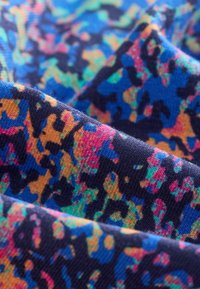 Tissu abstrait présentant un motif multicolore vibrant de bleu, d'orange et de rose sur un fond bleu marine profond, avec un tissage texturé.