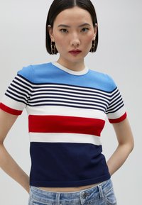 Randig kortärmad tröja i stickad kvalitet, med blå, vit, röd och marinblå färg. Har en rund halsringning och en matchande broderad logotyp vid fållen.