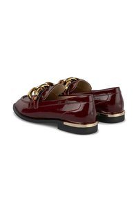 Bordeaux patentleren loafers met grote gouden kettingdetails en goudaccenten op de lage zwarte hakken, gezien vanuit de achterkant, schuin naar links.