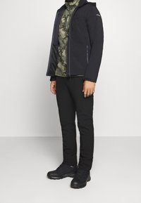 Veste isolée noire avec capuche, chemise camouflage en dessous, pantalon noir et chaussures de randonnée noires. Comprend des poches zippées et une finition texturée.