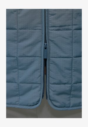 Kudumis sinine vest sileda pinnaga. Omab keskmist lukku koos kummist tõmblukupulgaga ning versioon on kaetud ruudustiku mustriga.