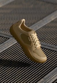 Beige sneaker with a mesh and synthetic upper, circular perforations, rounded toe, thick sole with protrusions, and subtle branding.