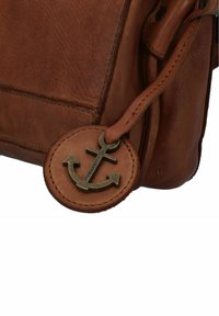 Borsa in pelle marrone con un'etichetta rotonda dotata di un design di ancoraggio impresso, che presenta una superficie texture e cuciture in contrasto.