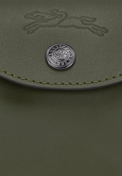 Grünes Lederetui mit strukturiertem Oberflächen, versehen mit einem eingeprägten Logo und einem runden Silberknopfverschluss. Kontrastierende Nähte heben das Design hervor.