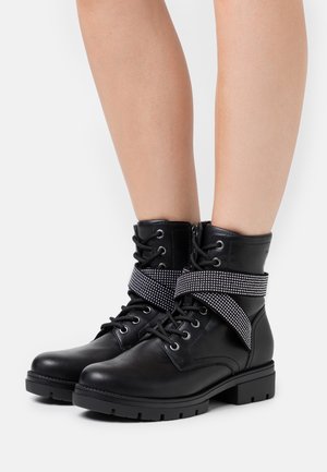 Stivali ankle in pelle nera con punta tonda, dotati di una cinghia con dettagli in swarovski e design con lacci, insieme a una suola in gomma testurizzata.