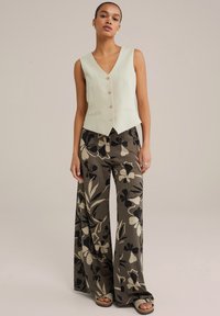 Svetlo zelena brezrokavna majica z V-izrezom in tremi gumbi, v kombinaciji z širokimi hlačami z vzorcem v temno zeleni barvi in cvetličnim dizajnom.