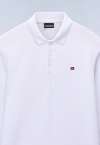 Polo blanc à manches courtes avec trois boutons, un petit emblème du drapeau norvégien sur la poitrine et une étiquette noire de la marque à l'intérieur du col.