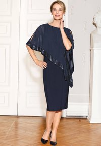 Marineblaues Kleid mit fließendem Cape, verziert mit Pailletten am Saum, figurbetontem Schnitt und glatter Stoffoberfläche.