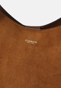 Borsa in suede marrone con rifiniture in pelle liscia e il logo dorato "COACH NEW YORK" ben visibile.