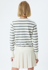 Sweter w paski w kolorze kremowym i szarym, z długimi rękawami i ściągaczem. Miękka tekstura, casualowy fason, w połączeniu z plisowaną spódnicą.