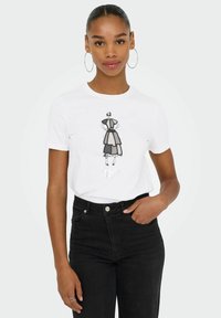 Hvid t-shirt med en sort og grå grafisk illustration af en modefigur med teksten "Selvtillid er nøglen." Båret med sorte jeans.