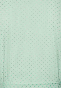 Tecido verde menta com uma textura subtil, apresentando bolinhas verdes escuras bem espaçadas. O material parece leve e suave.