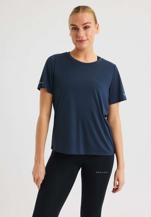 Marineblaues sportliches T-Shirt mit kurzen Ärmeln, runder Ausschnitt und glatter Textur. Mit einem Logo auf dem linken Ärmel. Getragen mit schwarzen Leggings.