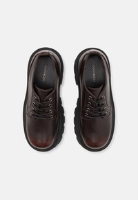 Scarpe in pelle marrone con finitura liscia, punta rotonda, design con lacci e suola in gomma nera con bordi texturizzati.