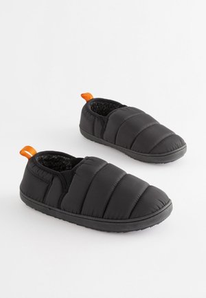 Zapatillas acolchadas negras con un forro suave y texturizado. Cuentan con una suela de goma negra y una lengüeta naranja en el talón para facilitar su uso.