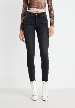Black skinny jeans with a high waist, featuring a faded texture and raw hem. Paired with white pointed ankle boots with studded accents.