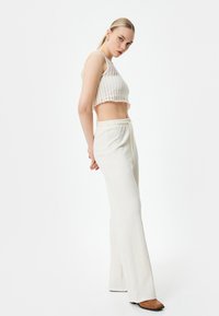 Top blanc, tricoté, à motifs carrés et coupé court ; associé à un pantalon clair, texturé, taille haute avec une ceinture élastique.