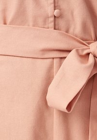 Różowa pastelowa sukienka o teksturowanej tkaninie, z wiązaniem w talii, detalami guzików i gładkim wykończeniem. Zaprojektowana w dopasowanym kroju.