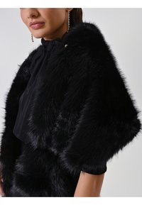 Châle en fausse fourrure noire avec une texture douce, présentant un design drapé et un col froncé. Accentué par un détail en métal doré.