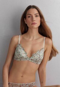 Bloemenkant bralette met een diepe halslijn en dunne verstelbare bandjes. Bevat complexe bloemenpatronen op een zachte, pastel achtergrond.