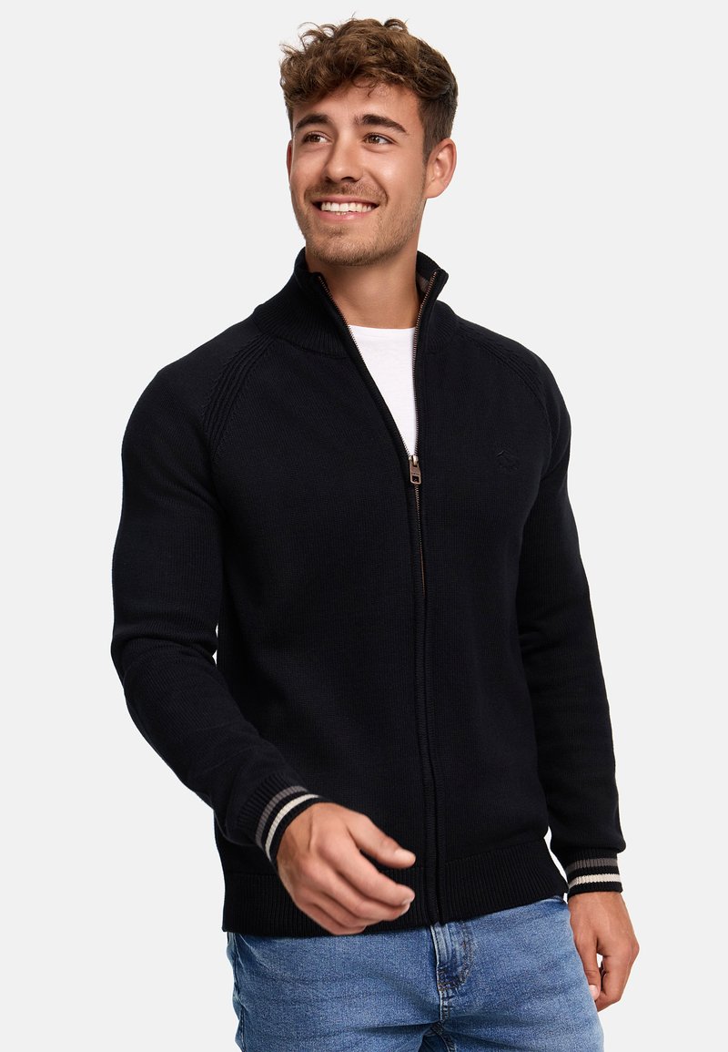 Sweat-shirt zippé noir en tricot avec un col haut, des poignets et un ourlet côtelés. Présente un logo discret sur la poitrine et un matériel de fermeture éclair neutre.